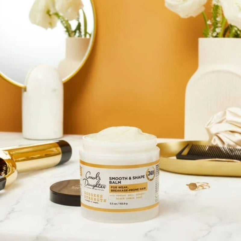 Carols Daughter hair smoothing and shaping balm jar on marble vanity with comb mirror and styling tools