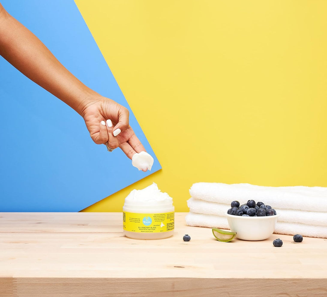 CURLS blueberry hair mask jar with creamy product on finger, blueberries bowl and towels