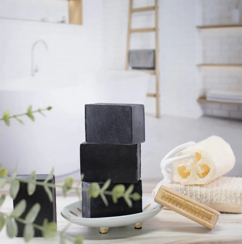 EARTH TO ME black charcoal cleansing bar soap stacked on ceramic dish with loofah brush and towel