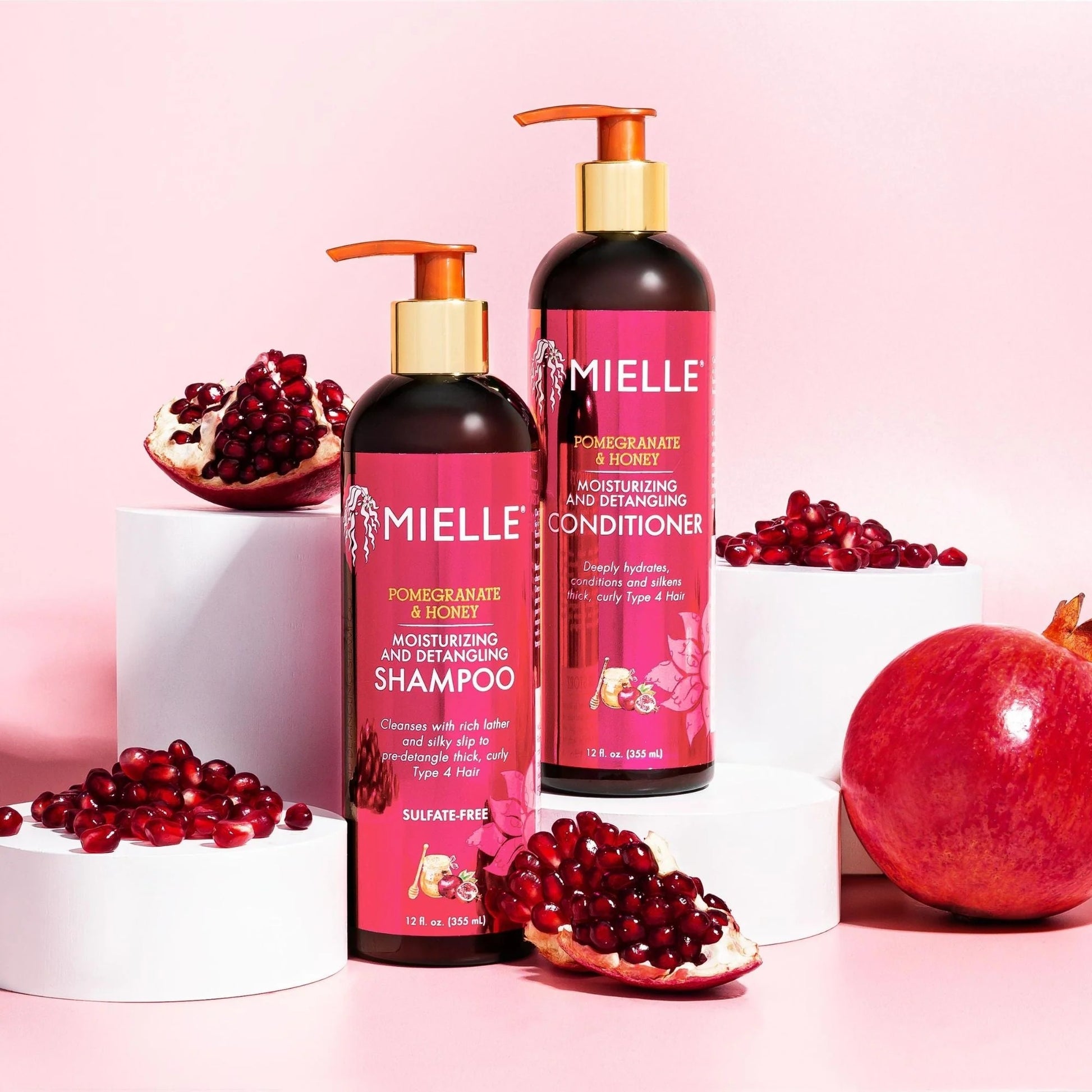 Mielle pomegranate honey leave-in conditioner bottle with shampoo and pomegranate seeds on pink background