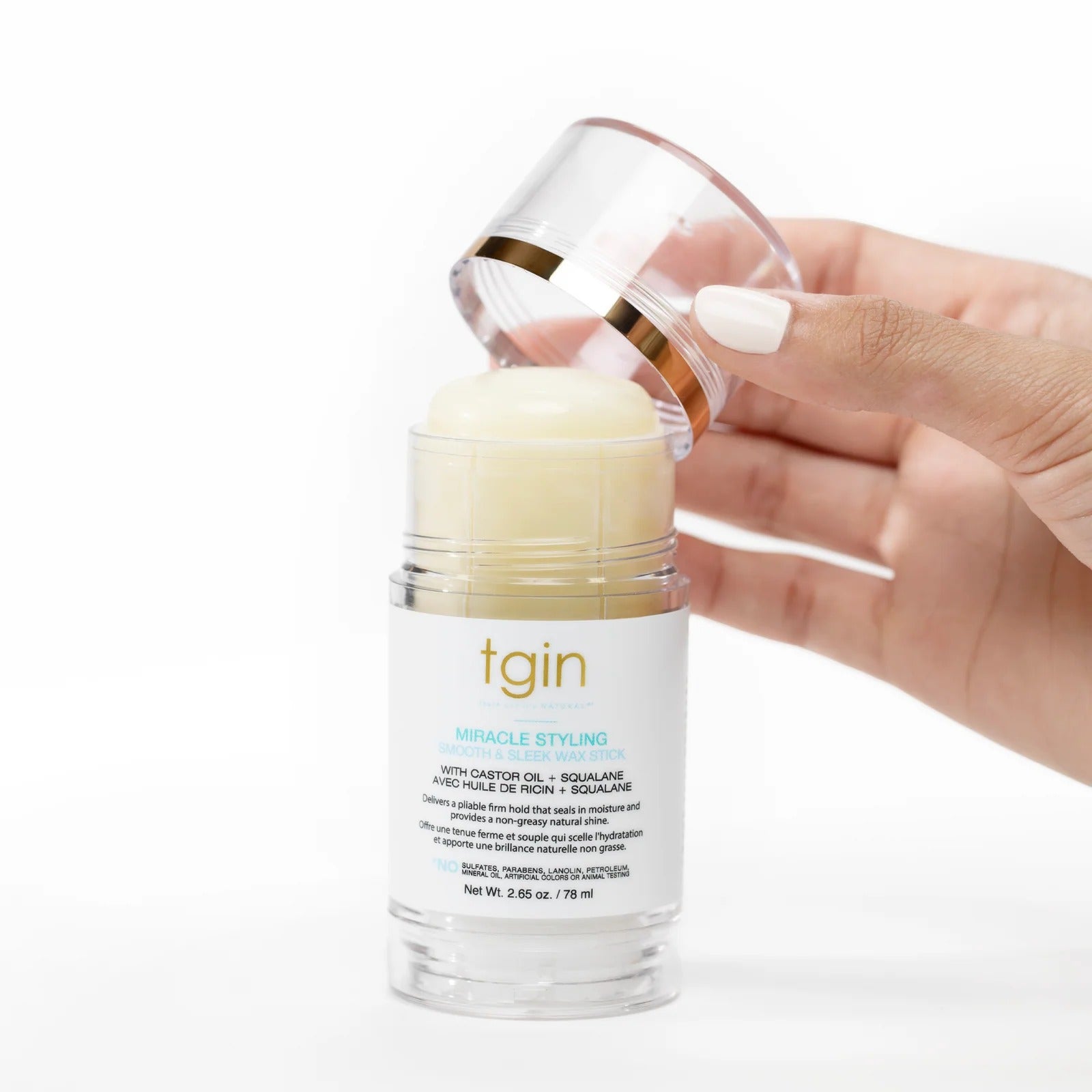 Hand removing cap from TGIN miracle hair styling wax stick in clear tube showing creamy stick